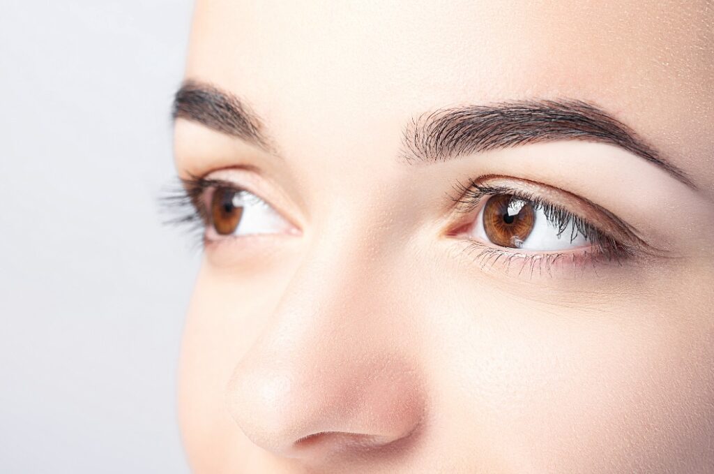 Woman with beautiful eyebrows close-up on a light background with copy space. Microblading, microshading, eyebrow tattoo, henna, powder brows concept