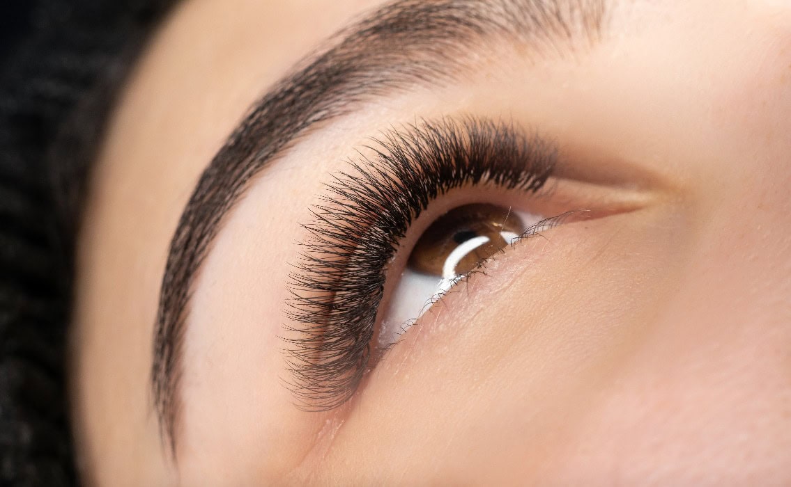 Weibliches Auge mit extra langen falschen Wimpern, Wimpernverlängerung und Augenbrauen-Tattoo. Make-up, Kosmetik, Schönheitskonzept. Nahaufnahme